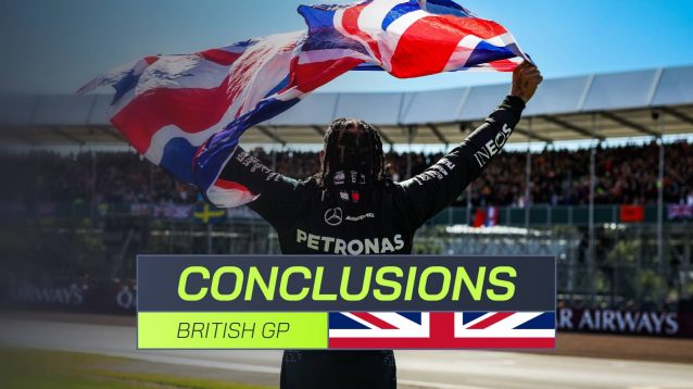 A shot from behind showing Lewis Hamilton raise a British flag to the crowd at Silverstone