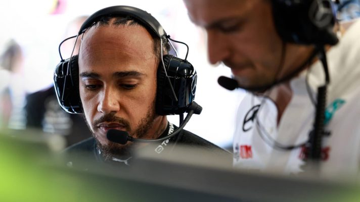 Lewis Hamilton sits wearing headphones at the central console in the Mercedes garage