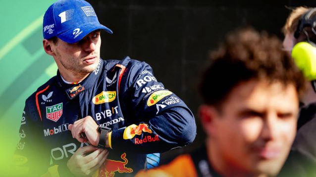 Max Verstappen looks on as he straps a watch to his wrist with Lando Norris blurry in the foreground