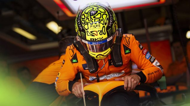 Lando Norris grips the halo as he lowers himself into his McLaren MCL38 in the garage at Monza