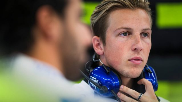Liam Lawson looks on in the VCARB garage with a blurry Daniel Ricciardo in the foreground