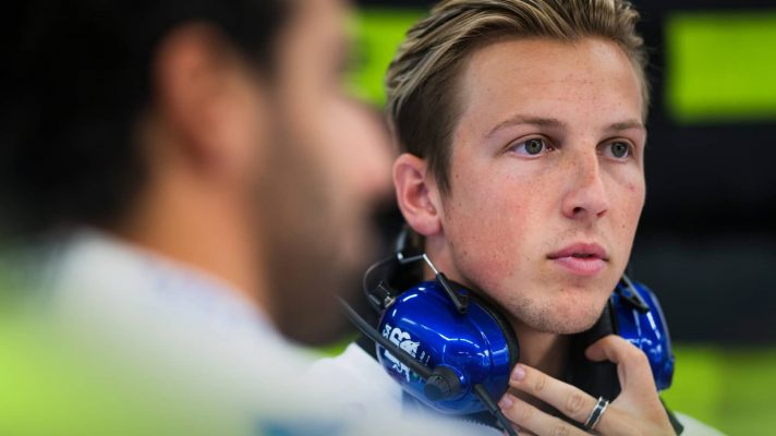 Liam Lawson looks on in the VCARB garage with a blurry Daniel Ricciardo in the foreground