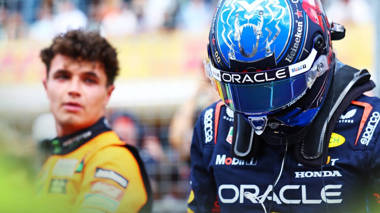 Lando Norris turns to look at Max Verstappen, whose helmeted head is lowered