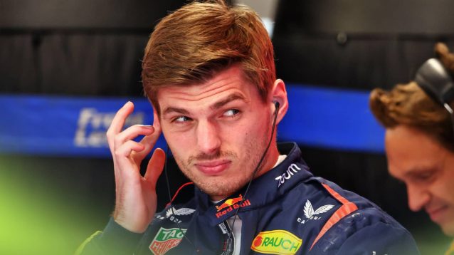 Max Verstappen pulls a face as he holds his finger to his ear in the Red Bull garage