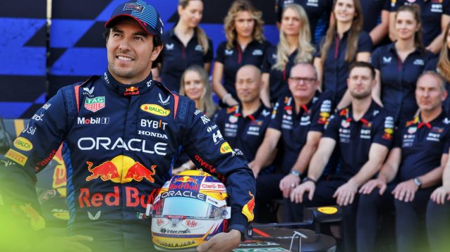 Sergio Perez poses with his helmet while sitting on the Red Bull RB20 with team staff in the background