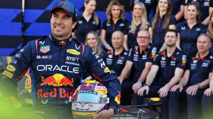 Sergio Perez poses with his helmet while sitting on the Red Bull RB20 with team staff in the background