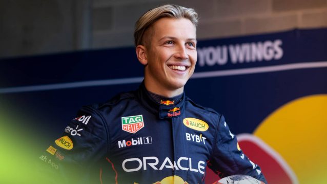 Liam Lawson smiled while wearing Red Bull Racing overalls in a garage