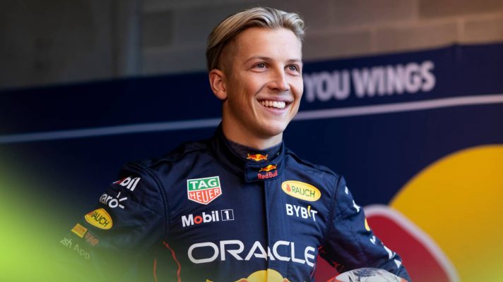 Liam Lawson smiled while wearing Red Bull Racing overalls in a garage