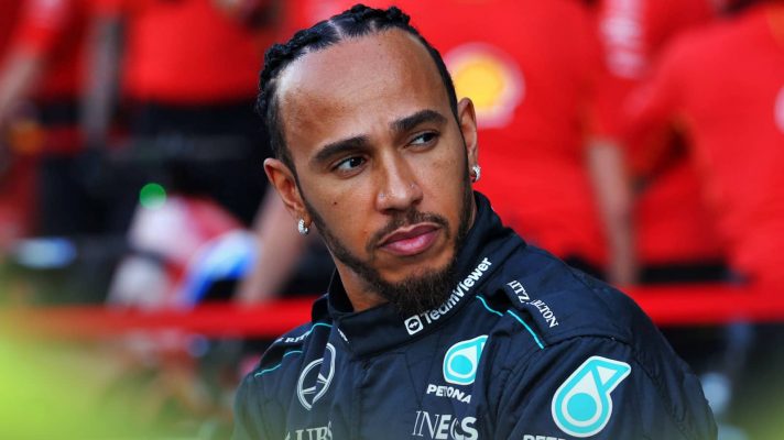 Lewis Hamilton looks over his shoulder during Mercedes' season-ending photocall with Ferrari mechanics working in the background