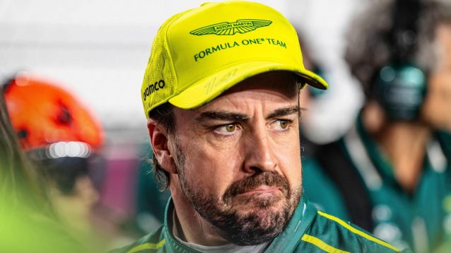 Fernando Alonso wearing a lime-green Aston Martin cap as he looks into the distance