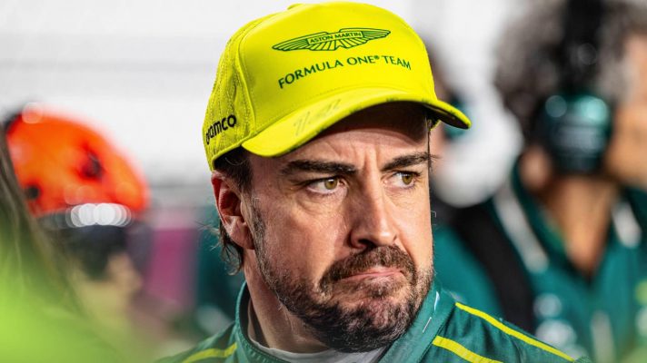 Fernando Alonso wearing a lime-green Aston Martin cap as he looks into the distance