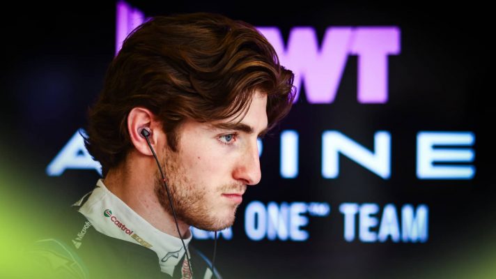 Jack Doohan looks glum in the Alpine garage with the team's logo in the background