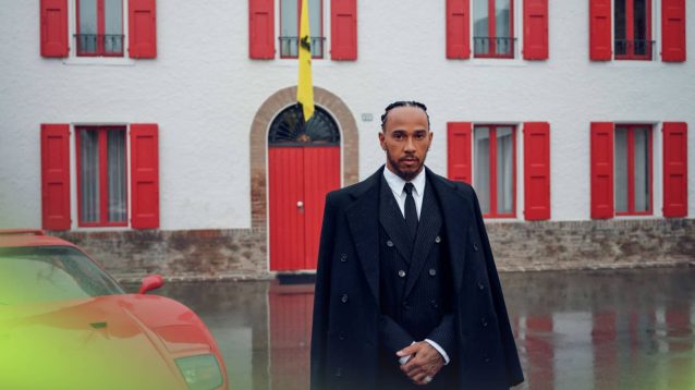 A suited and booted Lewis Hamilton poses outside of Enzo Ferrari's former office at Maranello