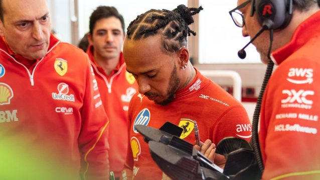 Lewis Hamilton looks deep in thought in conversation with a group of Ferrari engineers