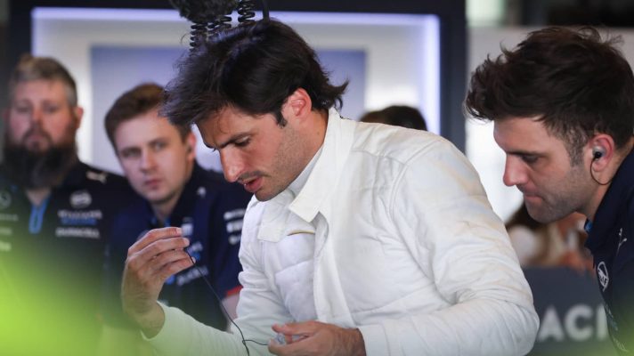 Carlos Sainz looks down in the garage with Williams mechanics looking on in the background