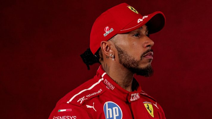 A studio shot of Lewis Hamilton looking into the distance while wearing a Ferrari race suit and cap