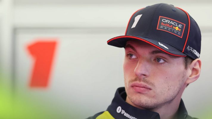 Max Verstappen looks on in the Red Bull garage with an image of a number 1 in the background