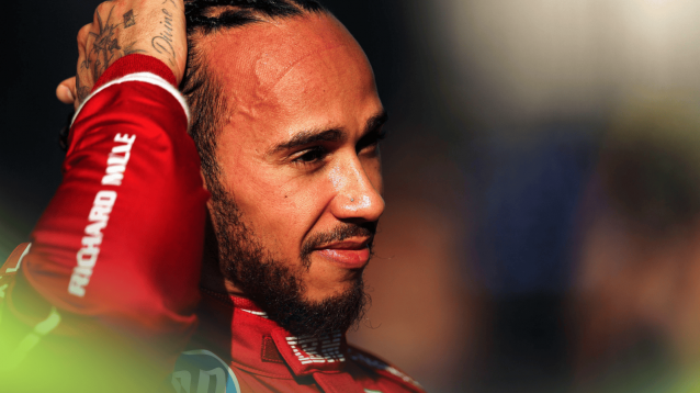 Lewis Hamilton smiles as he runs his hand through his hair