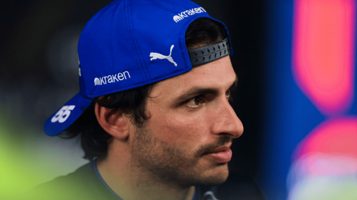 A side-profile shot of Carlos Sainz wearing his cap the wrong way around as he faces the media