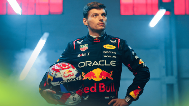 A studio shot of Max Verstappen wearing Red Bull overalls and clutching his 2025 race helmet