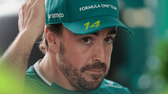 A close-up shot of Fernando Alonso wearing Aston Martin team kit in the paddock