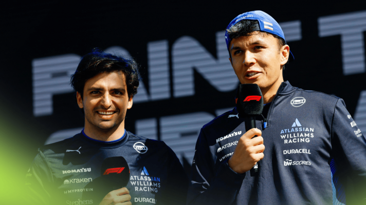 Carlos Sainz and Alex Albon holding microphones on stage at an event