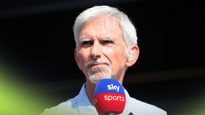Damon Hill holds a Sky F1 microphone against a dark background