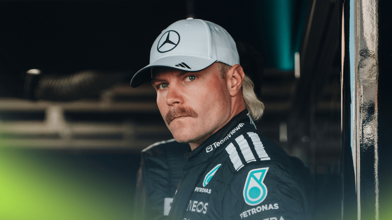 Valtteri Bottas eyes the camera while wearing black Mercedes race overalls and a grey cap