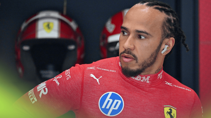 Lewis Hamilton looks on in the Ferrari garage with a row of mechanics' helmets in the background