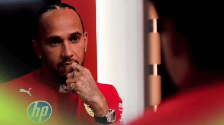Lewis Hamilton holds his hand to his face while sitting opposite Charles Leclerc