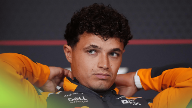Lando Norris adjusts his coat in a press conference