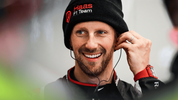 Romain Grosjean smiles as he inserts his ear plugs while wearing a Haas beanie hat