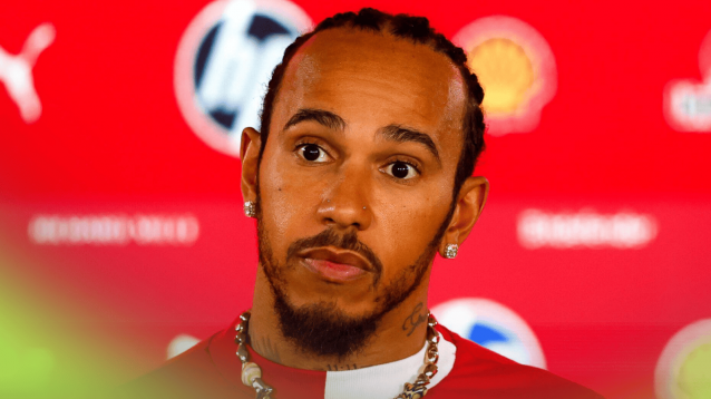 Lewis Hamilton looks alarmed as he faces the media with the logos of Ferrari's sponsors in the background