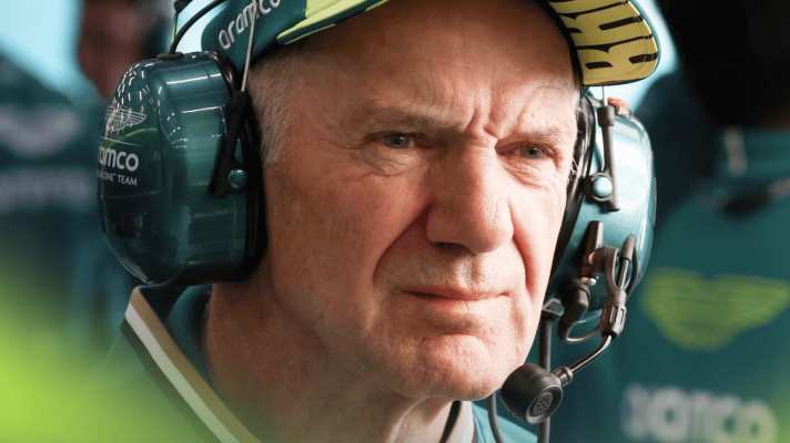A close-up shot of Adrian Newey wearing a cap and headphones in the Aston Martin garage