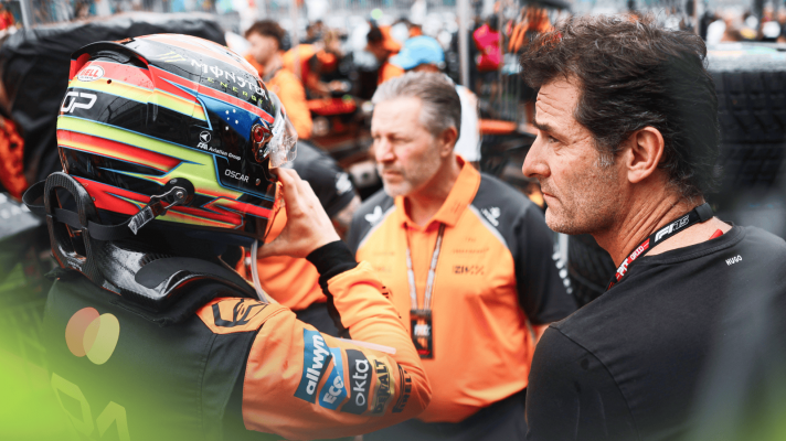 Oscar Piastri puts on his helmet on the grid as Mark Webber looks on with Zak Brown positioned in the middle