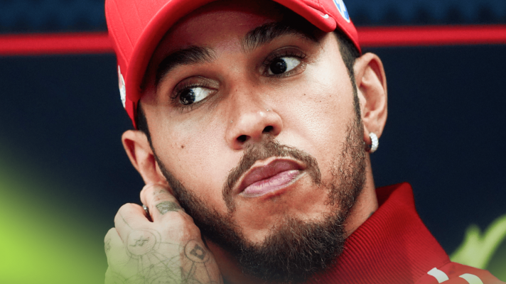 A close-up shot of Lewis Hamilton touching his ear in a press conference