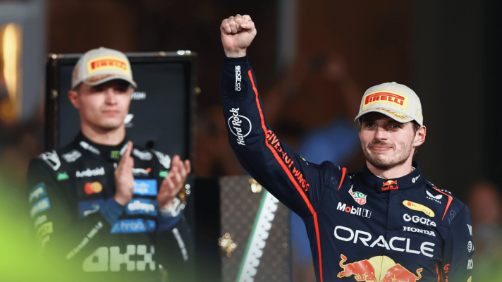 Max Verstappen holds an arm aloft on the Abu Dhabi Grand Prix podium as Lando Norris applauds in the background