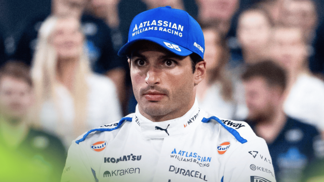 Carlos Sainz looks on during a Williams end-of-season photocall with faces of team staff in the background