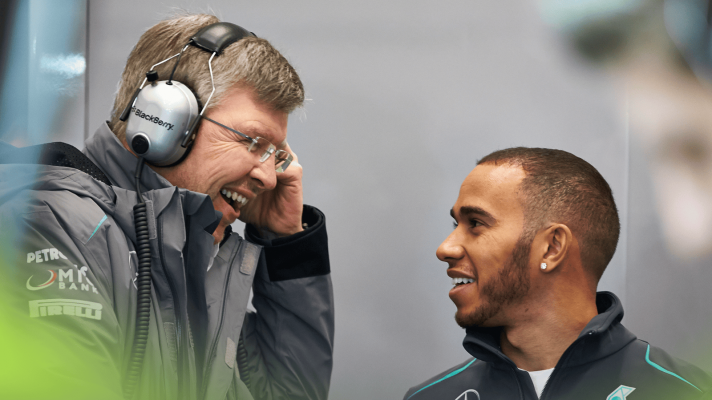 Ross Brawn and Lewis Hamilton laughing together in the Mercedes garage in 2013