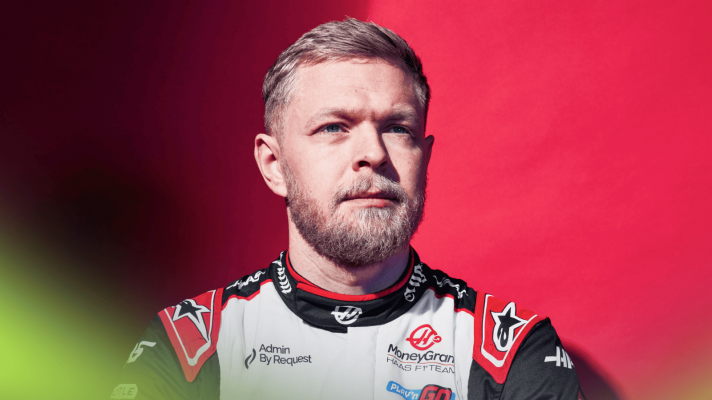 A studio shot of Kevin Magnussen looking on in Haas overalls against a red background