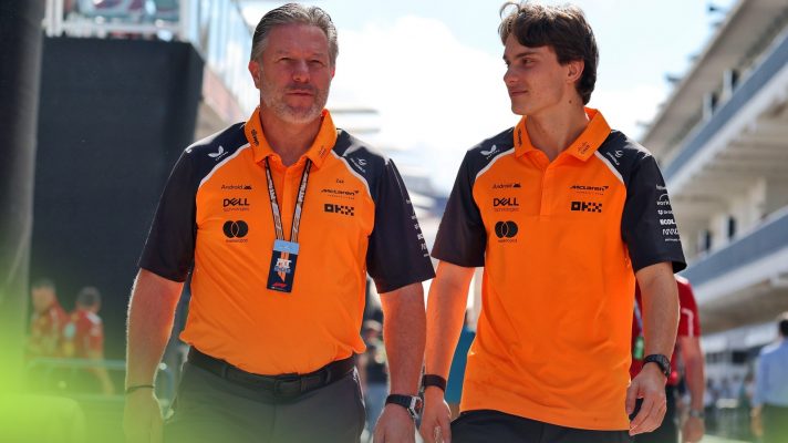 Zak Brown and Oscar Piastri walk towards the camera in the F1 paddock.