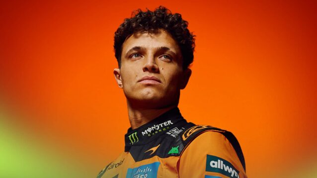 A studio-based shot of Lando Norris posing in McLaren 2026 overalls against a bright-orange background