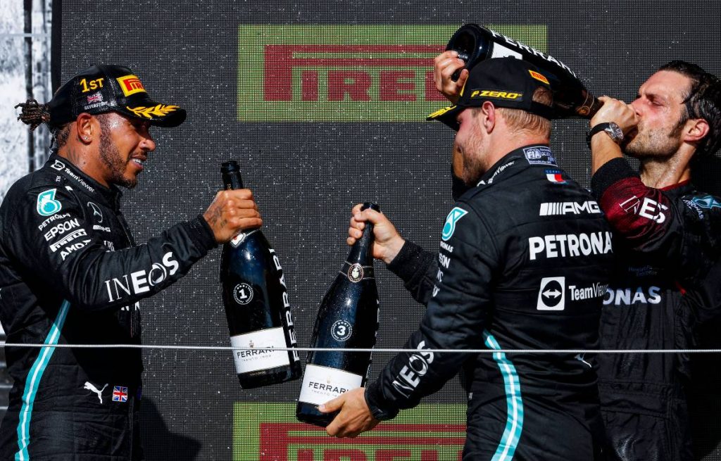 Lewis Hamilton and Valtteri Bottas clink bottles on the British GP podium. Silverstone July 2021.