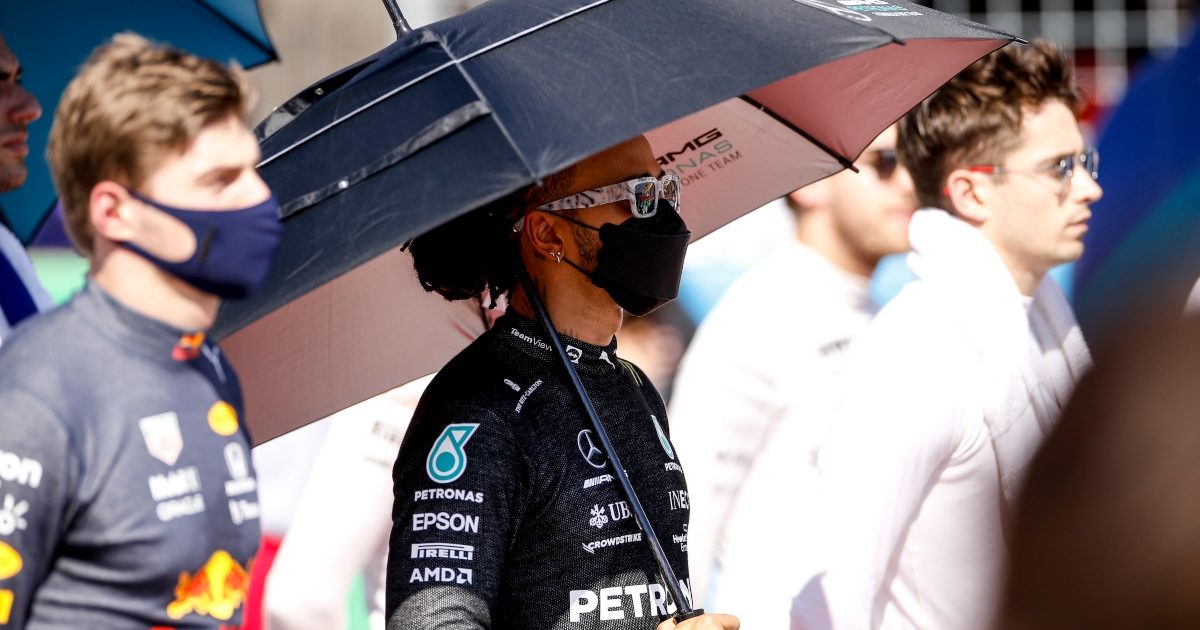 Lewis Hamilton standing between Max Verstappen and Charles Leclerc holding an umbrella. Austin October 2021