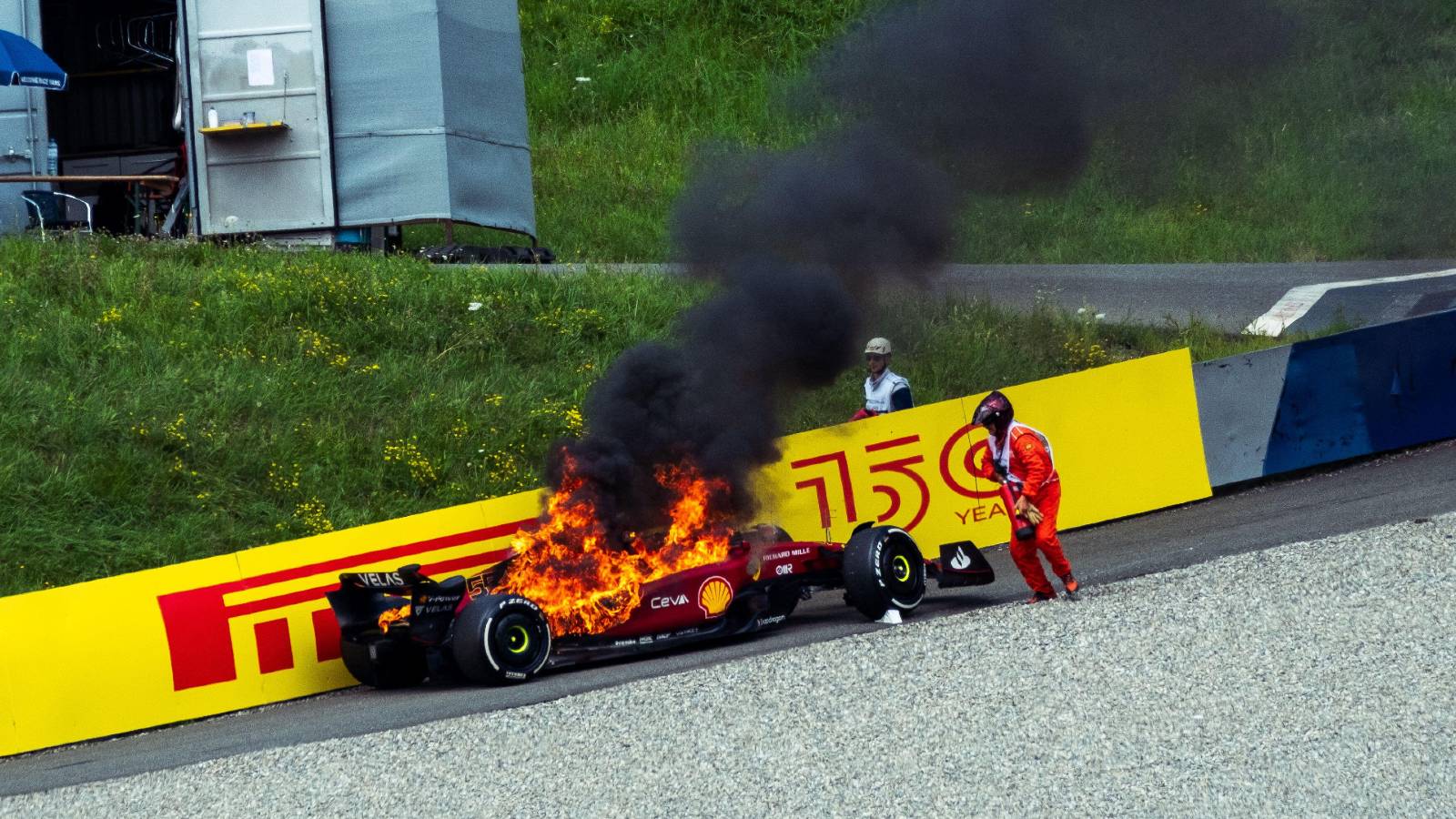 A marshal attends Carlos Sainz's burning Ferrari. Red Bull Ring July 2022.