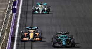 Lance Stroll's Aston Martin alongside Daniel Ricciardo's McLaren with Lewis Hamilton's Mercedes behind. Jeddah March 2022.