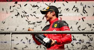 Charles Leclerc smiling while spraying Ferrari champagne on the podium at the Belgian Grand Prix