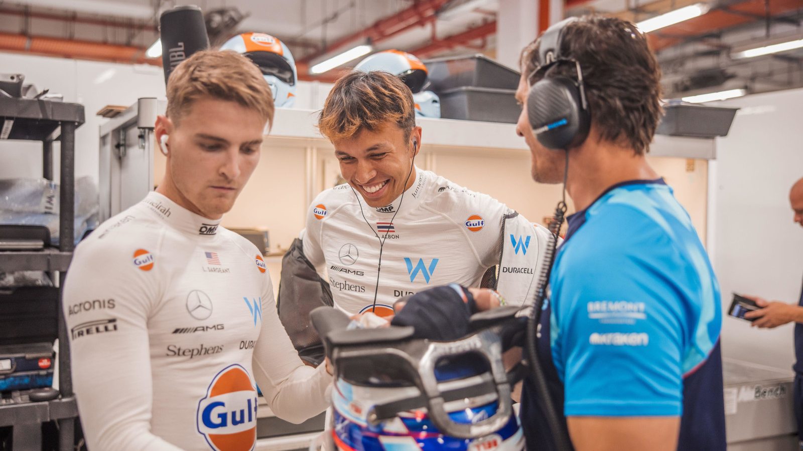 Alex Albon laughing in the garage while his teammate Logan Sargeant looks serious.