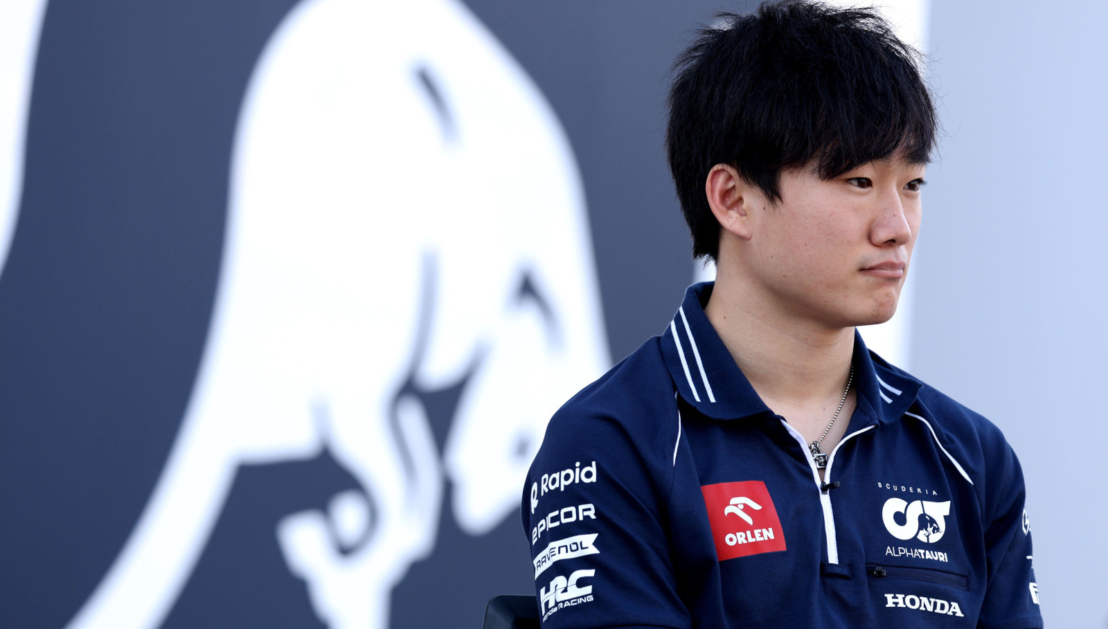 Japanese driver Yuki Tsunoda standing in front of the AlphaTauri logo.