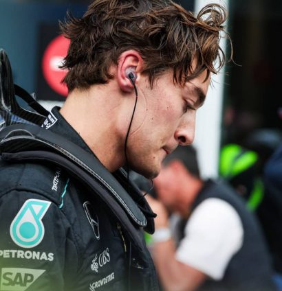 George Russell looks downbeat at the end of the Canadian Grand Prix as race winner Max Verstappen adjusts his cap in the background